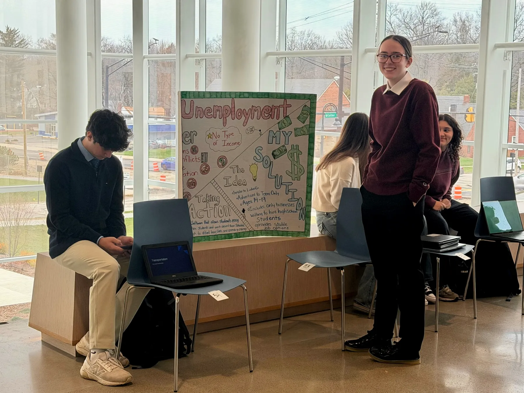 A student beside a poster project on unemployment in the Innovation Gallery at Barrier Breakers 2026